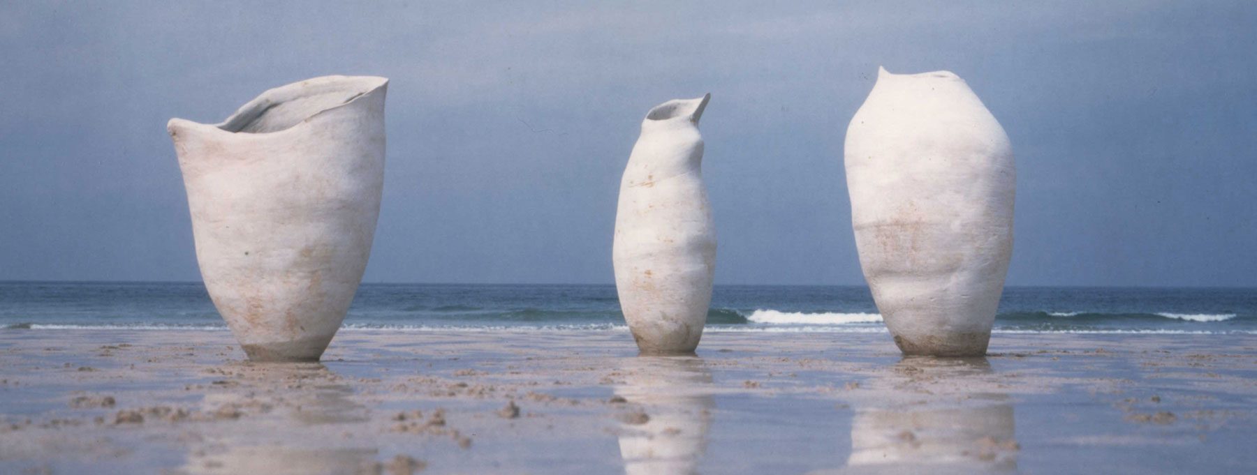 Three pale, hand-built vessels standing on a wet beach with the sea behind them