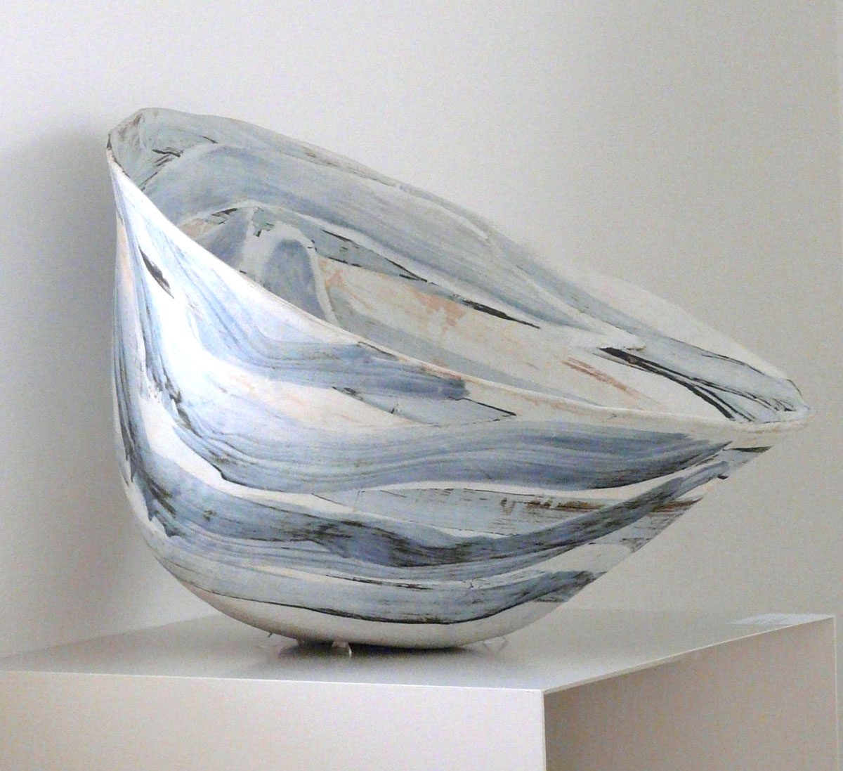 A tilted bowl with soft bands of blue-grey colour on a white plinth