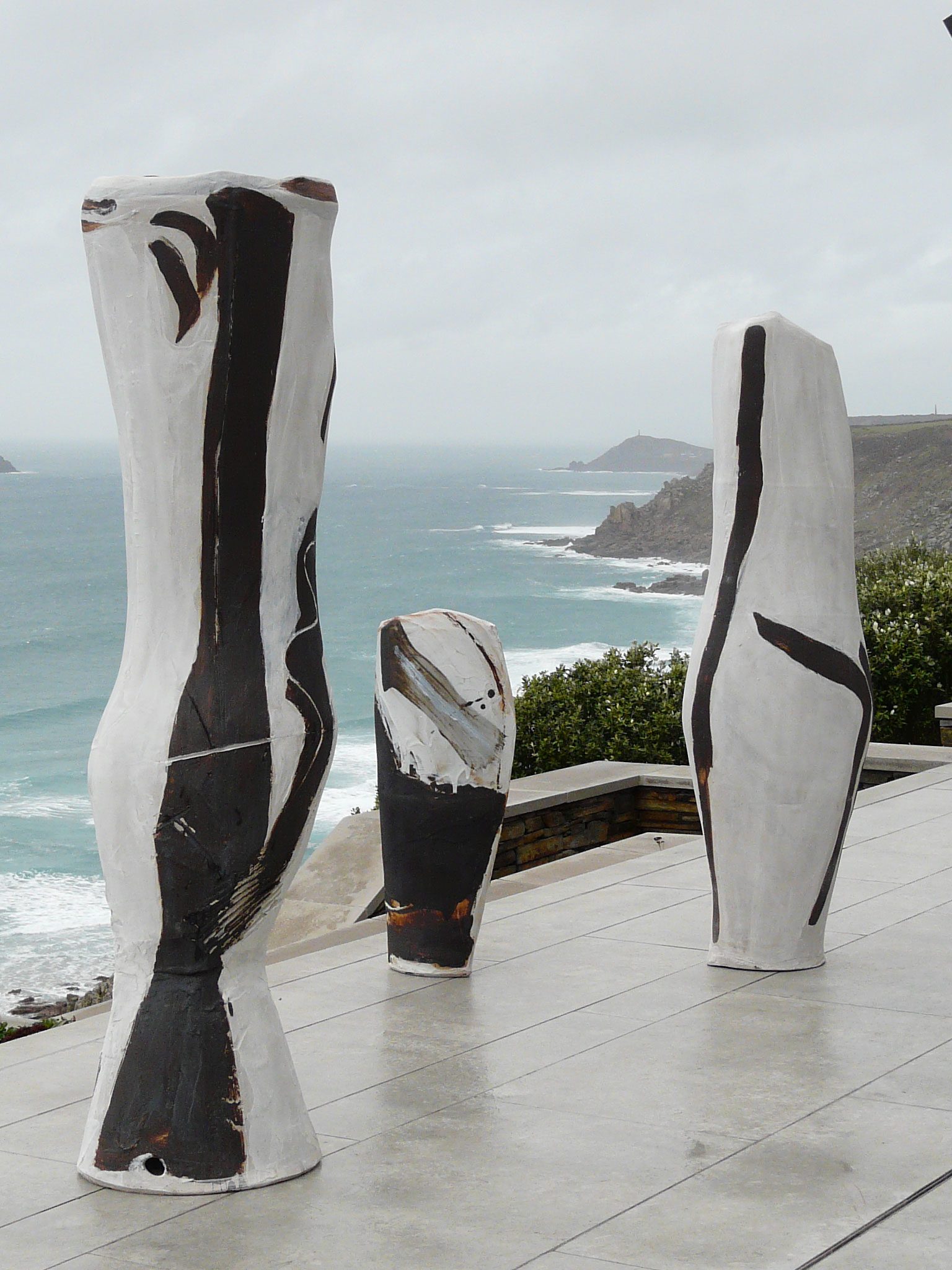 Three tall white vessels with bold black brushstrokes on a terrace above a stormy coast