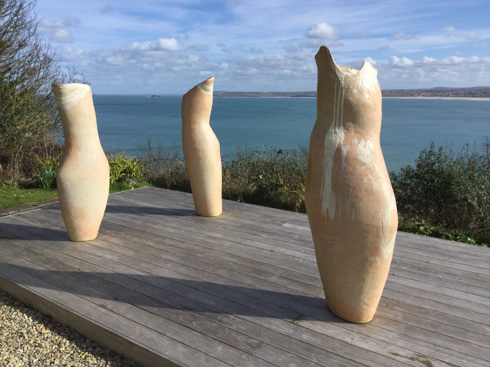 Three tall, pale vessels on a wooden deck above a blue bay