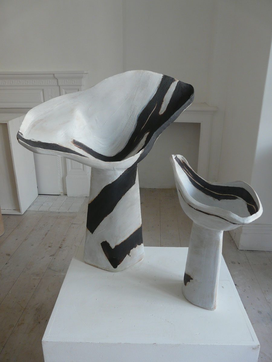 Two flared white forms with black stripes on a white plinth