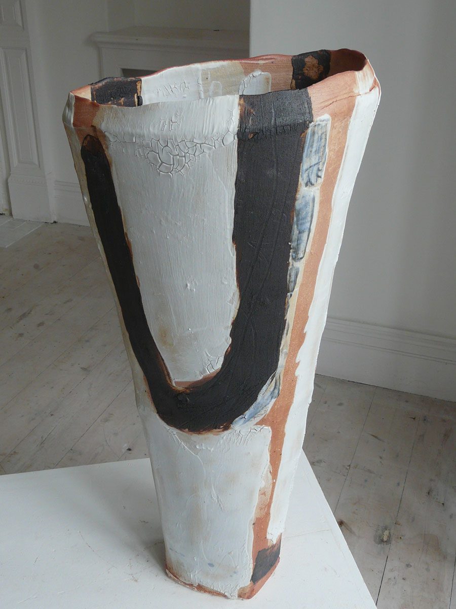 A tall tapering vessel painted white with a bold black U-shaped stroke and rust-red edges
